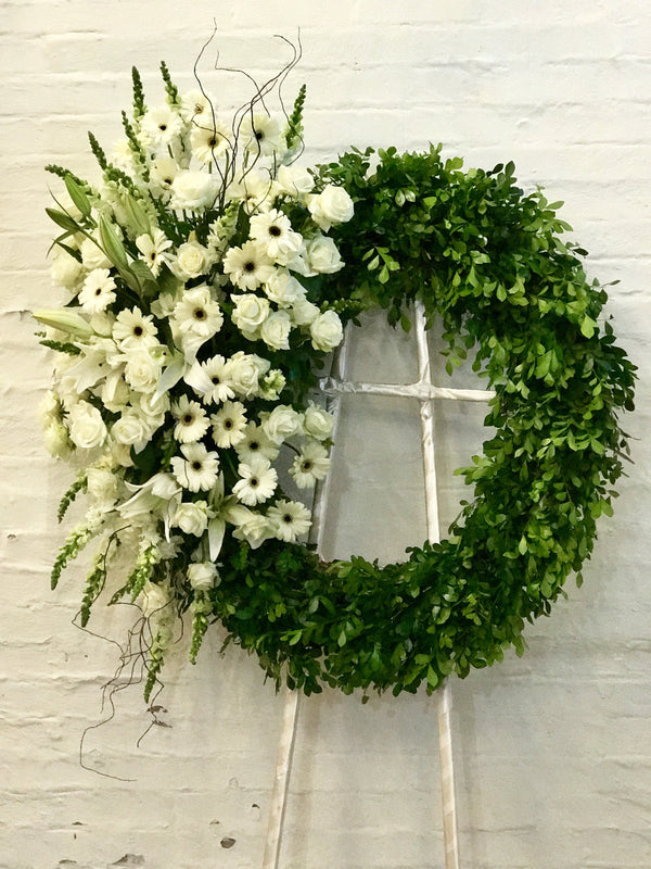 Fé, corona de follaje verde con flores blancas al costado